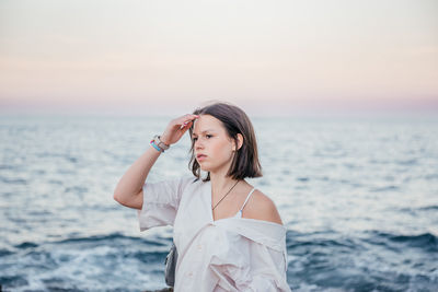 Young woman looking away while standing against sea