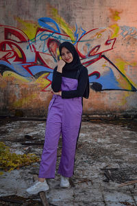 Full length portrait of young woman standing against graffiti wall