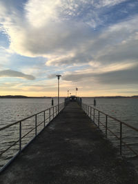 Pier over sea against cloudy sky at sunset