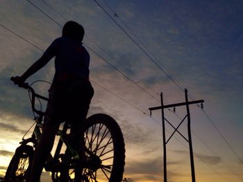 Low angle view of silhouette man with bicycle against sky