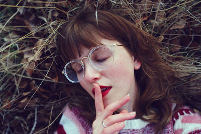 Close-up of young woman with finger on lips lying at field