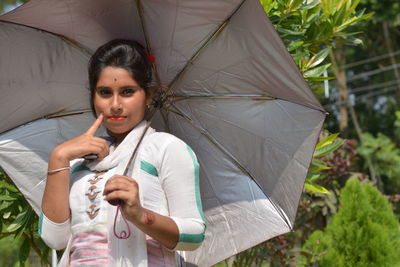 Portrait of young woman holding umbrella while standing outdoors