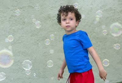 4-5 year old boy with curly hair in his backyard, playing with soap bubbles