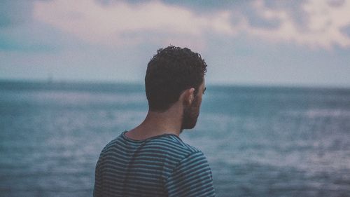 Rear view of man standing on beach against sky