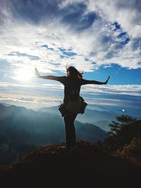 Rear view of woman standing with arms outstretched on mountain peak against sky