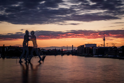 Silhouette of buildings at riverbank during sunset