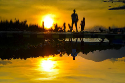 Silhouette couple at lakeshore against sky during sunset