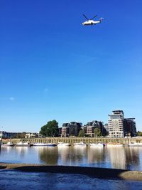 Low angle view of helicopter flying over lake against clear blue sky