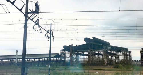 Low angle view of electricity pylon by building against sky