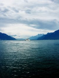 Boats sailing in sea against cloudy sky