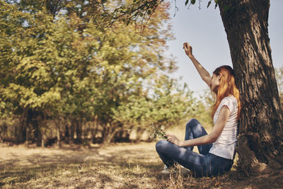 Young woman sitting on land against trees