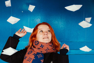 Smiling woman looking at paper boats hanging against blue wall