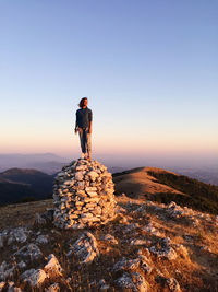 Full length of woman standing on mountain against clear sky at sunset