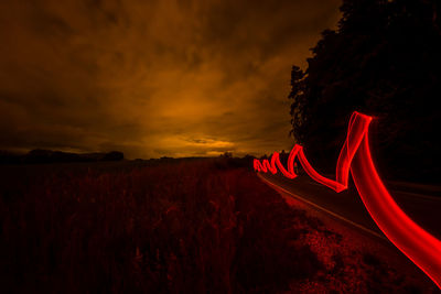 Red light trails on country road against cloudy sky