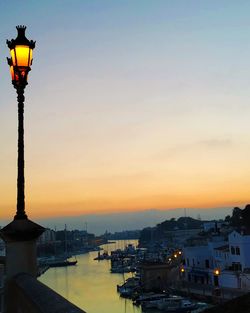 Illuminated street amidst buildings against sky during sunset