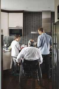 Rear view of disabled father in wheelchair with sons at kitchen