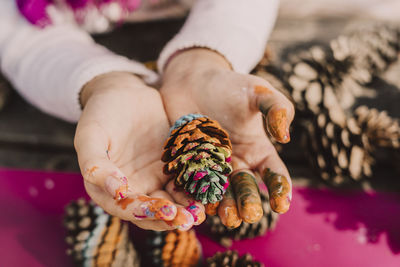 Messy hands of girl with colorful pine cone at picnic table in park