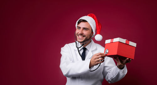 Young man smiling while standing against red background
