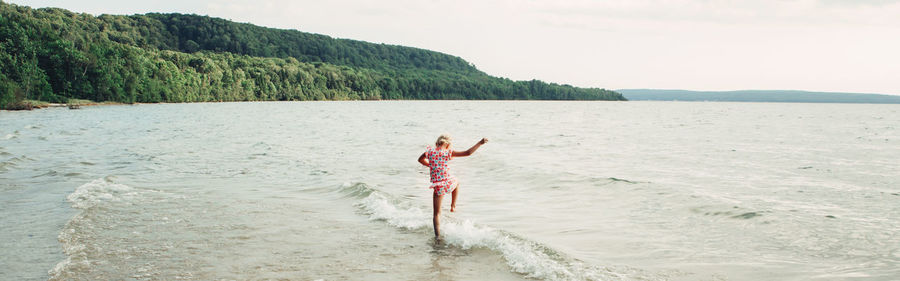 Rear view of woman standing in sea against sky