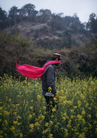 Rear view of person with yellow flowers on field