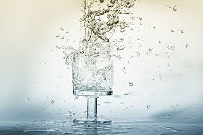 Close-up of water splashing in drinking glass against white background