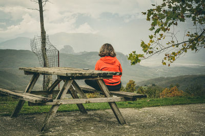 Rear view of man sitting on picnic table against mountains