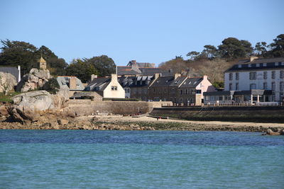 Buildings by sea against clear blue sky