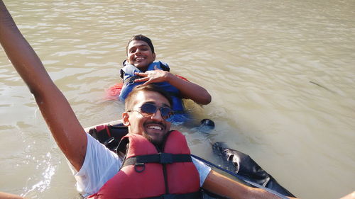 Happy friends wearing protective workwear floating in river