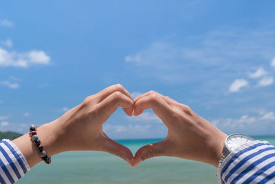 Midsection of man making heart shape against sky