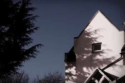 Low angle view of silhouette trees by house during sunny day