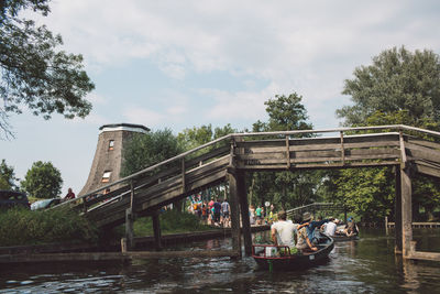 People on boats sailing in river below bridge against sky