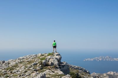 Rear view of man standing on rock by sea against clear sky