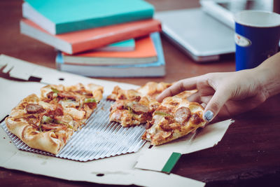 Close-up of hand holding pizza on table