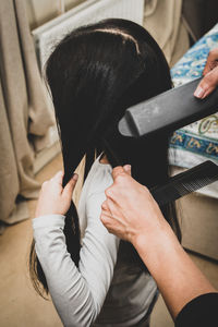 Cropped hand of hairdresser styling girl hair at home