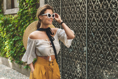 Young woman wearing sunglasses standing against wall