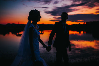 Silhouette couple standing against orange sky during sunset