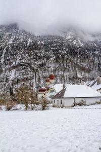 Snow covered houses on field by buildings against sky during winter