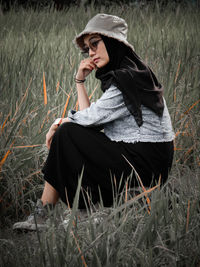 Young woman looking away while sitting on land