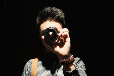Close-up of man holding lens against black background