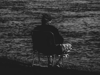 Rear view of man sitting on chair at beach