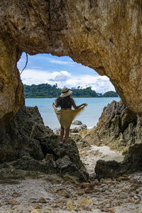 Rear view of woman standing on rock by sea