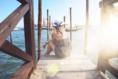 Rear view of woman sitting on pier during sunny day