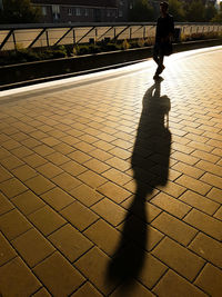 Silhouette person walking with shadow on footpath
