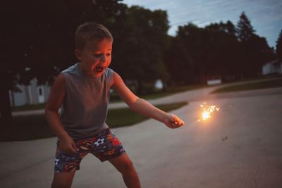 Boy holding sparkler at park during dusk