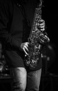 Midsection of man playing saxophone in darkroom