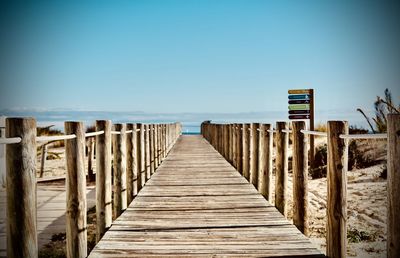 Wooden pier on beach against clear blue sky
