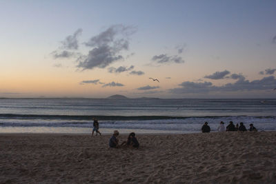 People on beach against sky during sunset