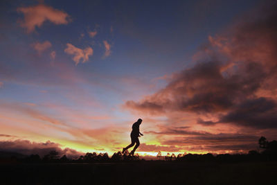 Silhouette person running on land against cloudy sky during sunset