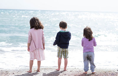 Rear view of children standing on shore at beach