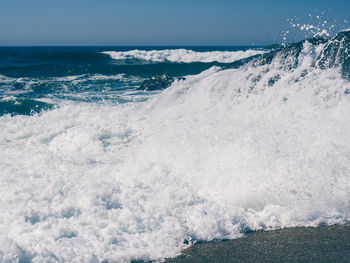 Waves splashing on shore against sky